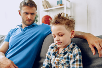 Father is having a talk with his little son while sitting on couch at home