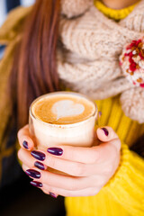 Latte in a transparent glass in the hands of a girl in a bright New Year's sweater