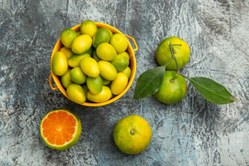 Overhead view of a yellow bucket full of fresh green tangerines and cut in half tangerines on gray background