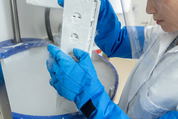 Herausnahme von eingefrorenen Zellen aus Kryokonservierung Tank mit Schutzhandschuhen und Gesichtsschutz.