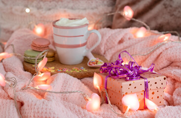 Valentine's Day at home. Blurred cup with cream. Spoon with heart-shaped sweet confetti - close-up on a gift box, background with pink lights