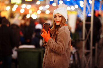 Fototapeta na wymiar beautiful girl on the background of lights with coffee, on the street, holiday, new year. a walk through the evening city smiles