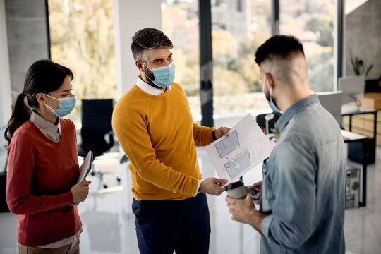Group of architects wearing face masks while analyzing blueprints in the office.