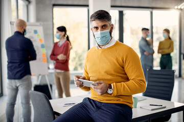 Mid adult businessman working on touchpad and wearing protective face mask in the office.