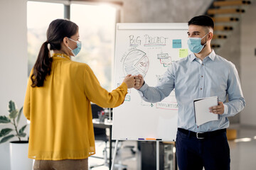 Obraz premium Business colleagues fist bumping while wearing protective face masks in the office.
