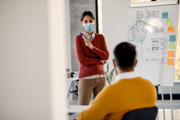 Casual businesswoman wearing face mask while giving presentation on whiteboard in the office.