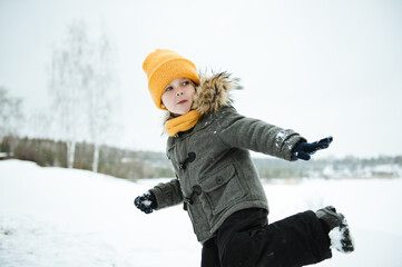 Cute a boy in warm yellow hat and gray overcoat walking in winter the forest.