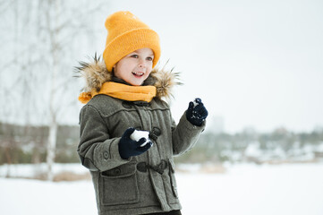 Fototapeta na wymiar Cute a boy in warm yellow hat and gray overcoat walking in winter the forest.