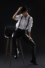 Beautiful fashionable young woman sitting on chair against dark background