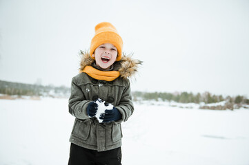 Fototapeta na wymiar Cute a boy in warm yellow hat and gray overcoat walking in winter the forest.