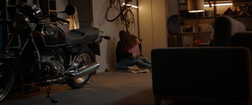 HANDHELD Teenagers kissing passionately, sitting on a floor inside a garage, having an intimate moment. Shot with 2x anamorphic lens