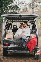 Happy young couple in love sitting in a van decorated with festive Christmas lights, hugging and laughing.