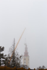 Team of construction workers in crane basket under deep winter fog  putting new cross on the top of St. Simon and Jude Thaddeus church in Zagreb, Croatia