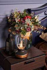 beautiful winter bouquet with flowers and Christmas balls on a bedside table in a vase made of transparent glass. there is a lamp with a retro lamp nearby