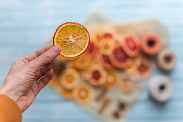dried orange slice in a hand for diy projects, gift wrapping and beautiful eco Christmas decorations like wreaths, more decoration items arranged on a blue wooden table in the background - 400151756
