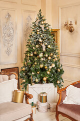 a beautiful fluffy tree with slightly snow-covered branches decorated with large golden balls and feather-shaped toys stands in the corner of a room with light walls. there are boxes with gifts under 