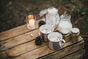 Hot cocoa with melted marshmallows and cinnamon on wooden table nearpot with milk.