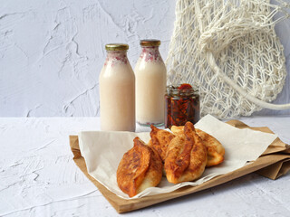 Appetizing homemade fried pies on kraft papers and yogurt in bottles on white background