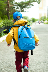 A little boy with a blue backpack hurries to school.