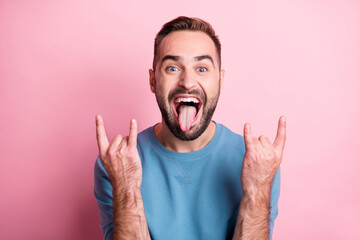 Photo of rude funky young guy wear blue pullover showing hard rock sign open mouth tongue isolated pink color background