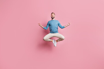 Full length photo of strong adorable young man dressed blue sweater jumping high practicing yoga isolated pink color background