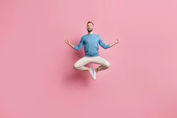  Volledige foto van een sterke schattige jongeman gekleed in een blauwe trui die hoog springt terwijl hij yoga beoefent, geïsoleerde roze kleur achtergrond © deagreez