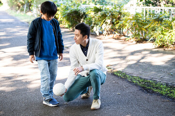 息子と仲良く公園でサッカーをする父親 © Monet
