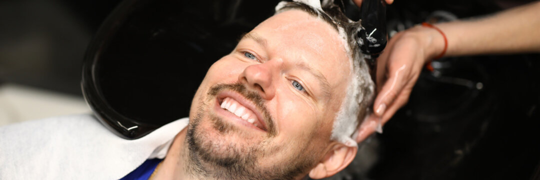 Portrait of smiling man who is being washed with shampoo in salon by master. List of services in beauty salons and hairdressing salons concept