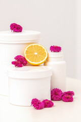 White cosmetic jars, containers, bottle with fresh lemon and chrysanthemums flowers on white background with copy space. Blank space for branding mockup beauty product