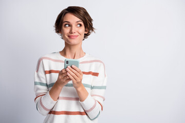 Photo of dreamy tricky lady wear striped sweater holding modern gadget looking empty space isolated grey color background