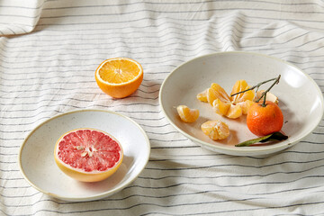 food, healthy eating and fruits concept - close up of mandarin, grapefruit and orange on plates over drapery