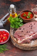 Vertical view of red meat on wooden tray and garlic green ketchup and chopped pepper oil bottle on dark background