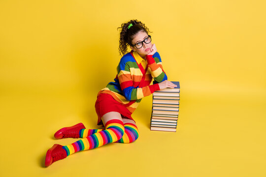 Photo of pretty student lady sit floor sad moody lean copybook pile wear rainbow print clothes isolated yellow color background