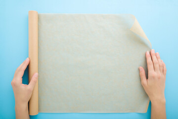 Young adult woman hands using roll of baking paper on light blue table background. Pastel color....