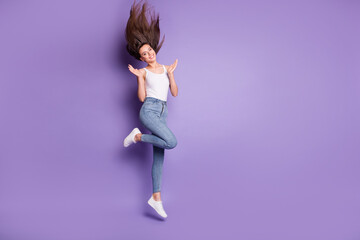 Fototapeta na wymiar Full size photo of slim happy brown haired woman jump up wear jeans raise palms isolated on purple color background