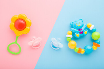 Flower rattle for baby girl and bear with balls for baby boy and soothers on light pink blue table background. Pastel color. Closeup. Top down view. Two sides.