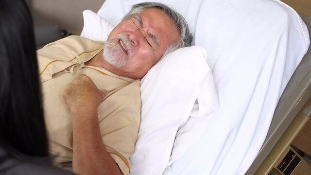Asian senior male patient lying on the bed in recovery room at modern hospital talking to his daughter about heart disease symptom. Hospital medical center and family healthcare insurance concept.