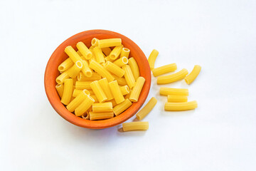 Uncooked raw Italian rigatoni pasta in an earthenware bowl on isolated white background.
