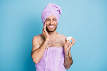 Portrait of nice cheerful guy wear turban towel applying cream smoothing effect perfection isolated on bright blue color background