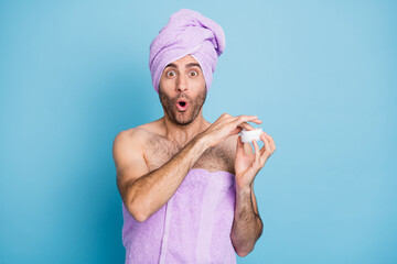 Portrait of nice cheerful amazed guy wear turban towel applying cream anti wrinkles effect isolated on bright blue color background