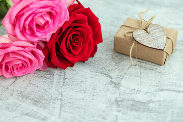 Gift wrapped in craft paper next to bouquet of roses on white stone background. Romantic gift for valentine's day with space for text. Marriage proposal concept. Copy space