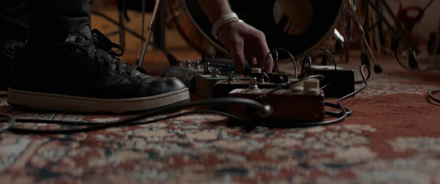 CU view of male musician guitarist pressing guitar effect pedals during rehearsal. Shot with 2x anamorphic lens