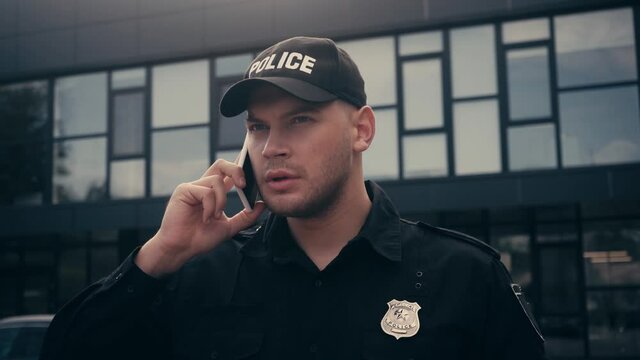 Policeman in uniform and badge talking on smartphone on urban street