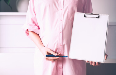 Pregnant woman with empty white paper as medical card, agreement blank. Template for text.