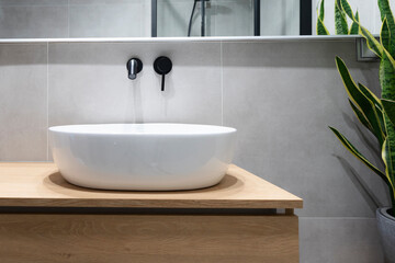 Stylish wash basin and tap in industrial interior of bathroom. Grey tiles and mirror and wooden...