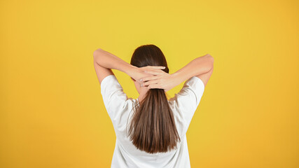 Yong woman shows off her long, straight dark hair on yellow background. Woman stands with her back and touches her hair, healthy even cut. Hair care for health and beauty.