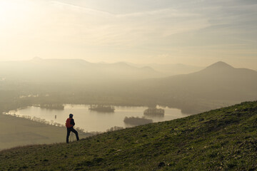 Male hiker looking at rolling landscape and hills of Czech Central Mountains at sunset