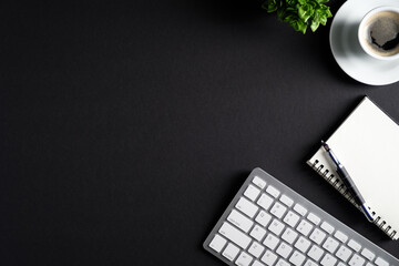 Black office desk table with cup of coffee, computer keyboard, notepad and pen. Flat lay, top view, copy space. Luxury, minimalist style workspace. Business concept.