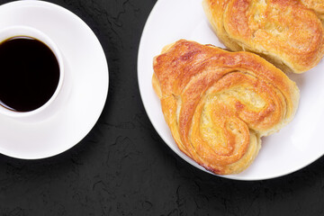Pastry on a white plate and cup of coffee on a black background. Homemade cake. Fresh baked cake. Breakfast.