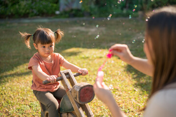 Selective focus, Happy family concept, Mother and lovely daughter blowing soap bubbles in the garden. little girl on the wooden rocking horse.